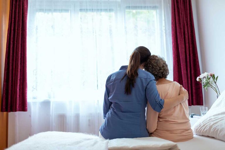 Assisted living staff member helping an older adult with daily activities in a comfortable residential setting.